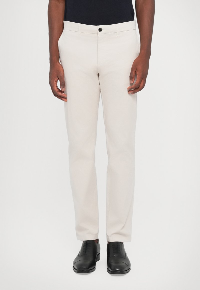 Pantaloni beige deschis dintr-un amestec de bumbac, cu croi drept, închidere frontală cu nasture, cu buzunare laterale și la spate, asortați cu pantofi negri.
