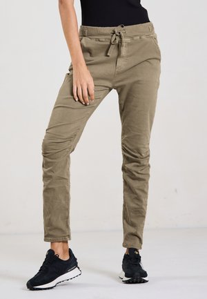Khaki Jogginghosen mit Kordelzugbund, schmal zulaufenden Beinen und dezenten Raffungselementen. Getragen mit schwarzen Sneakern.
