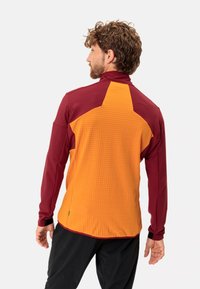 Langärmlige Jacke mit hohem Kragen, oberer Abschnitt in Bordeauxrot und unterer Abschnitt in einem strukturierten, hellen Orange, mit Kontrastnähten und Bündchen.