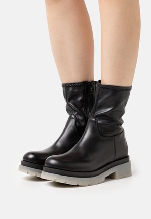 Stivali alla caviglia in pelle nera con un design morbido, cerniera laterale e suola in gomma grigia. Presentano dettagli con cuciture e un logo sul tallone.