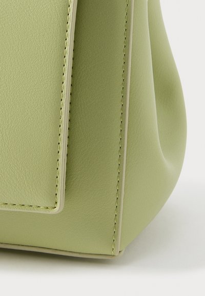 Πράσινη τσάντα χειρός από τεχνητό δέρμα με λεία υφή, ορθογώνιο καπάκι και αντίθετες ραφές. Διαθέτει στρογγυλεμένη βάση και ελάχιστα μεταλλικά στοιχεία.