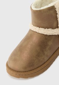 Bota de tornozelo castanha com um forro e acabamento macios e peludos, exterior texturizado e uma sola de borracha com um detalhe trançado.