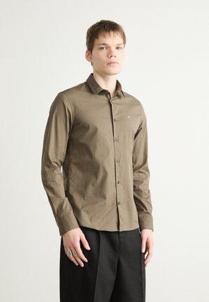 Camisa de manga larga verde oliva con cuello abotonado, que presenta un sutil logotipo en el pecho y botones negros, fabricada en tela de algodón texturizada.
