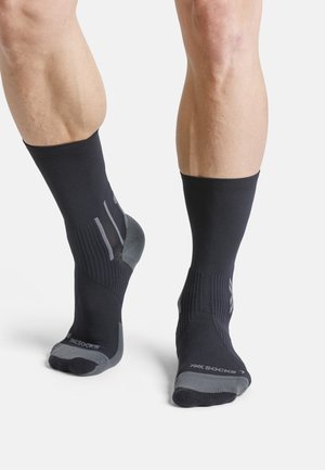 Legs wearing black and gray athletic compression socks with ribbed texture, one foot flat and the other raised on toes against white background.