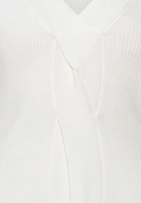 Top blanc à côtes avec un décolleté en V, détail croisé à l'avant et tissu texturé. Sans ornements, sans quincaillerie ni motifs visibles.
