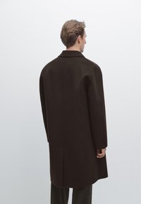 Brun uldfrakke med en afslappet pasform, der har krave, lige snit og lange ærmer. Ingen synlige lommer eller lukninger.