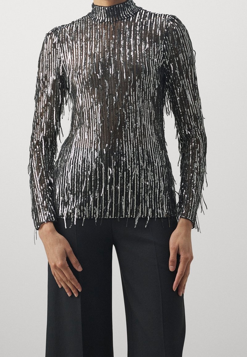 Schwarz-silbernes Langarmoberteil mit Fransen-Detail, hoher Kragen und transparentem Design mit vertikalen Paillettenstreifen.