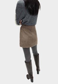 Bruine minirok van imitatiebont met hoge taille, gecombineerd met grijze geribbelde panty's en kniehoge bruine laarzen met hak. Grijze trui met mouwen in blokkleuren.