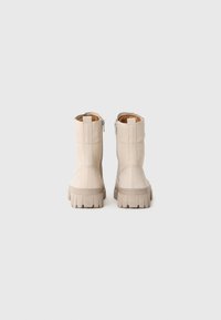 Botas de tobillo de ante beige con suela texturizada, cremallera lateral y costuras reforzadas. Diseño minimalista con una apariencia sólida y robusta.