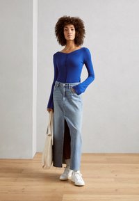 Blå ribbestrikket langermet topp med knapplukking, kombinert med et høyt liv denimskjørt med split foran, og hvite sneakers.