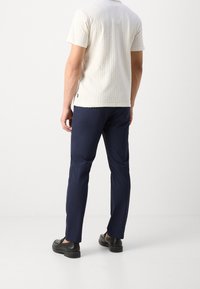 Witte gestructureerde short-sleeve shirt, marineblauwe slim-fit broek en zwarte schoenen. Het shirt heeft een ruitpatroon en een ronde hals.