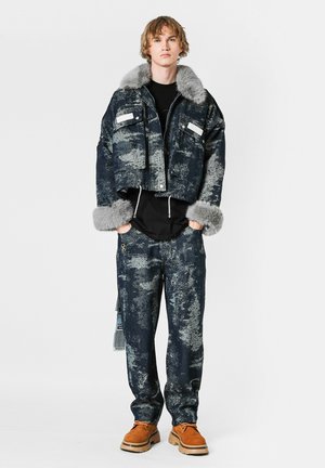 Chaqueta de mezclilla recortada con cuello de piel gris, tela azul oscura con un patrón abstracto claro. Pantalones holgados a juego, combinados con zapatos marrones.