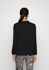 Haut noir à manches longues avec un col, doté de poignets froncés. Porté avec un pantalon taille haute à imprimé zèbre noir et blanc.