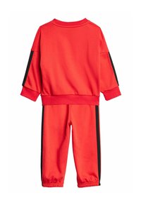 Czerwony zestaw bluz i spodni, wykonany z miękkiego materiału. Posiada czarne pasy boczne i ściągacze przy mankietach. Prosty, sportowy design.