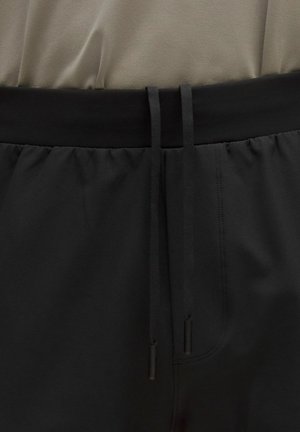 Fekete rövidnadrág széles, elasztikus derékpánttal, amelyen húzózsinórok vannak, sima anyagból és finom varrássel.