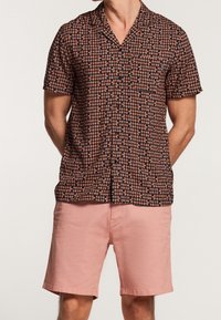 Koszula z krótkim rękawem o czarnym tle, z kolorowym wzorem liści. W połączeniu z jasnoróżowymi szortami, prezentującymi swobodny, luźny krój.