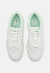 Baltos Calvin Klein Jeans sportbačiai su mėtos žalumos vidine pamušalu, baltais raišteliais ir logotipu ant vidpadžių bei liežuvėlių, matomi iš viršaus.