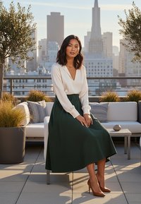 Biała bluzka z długim rękawem i dekoltem w kształcie litery V, w komplecie z ciemnozieloną spódnicą midi z paskiem. Brązowe buty na wysokim obcasie dopełniają stylizację.