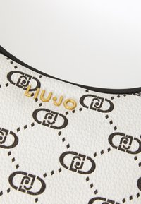 Hvid tekstureret lædertaske med et sort kædemønster og guld "LIU·JO" logo, med en sort kant langs den øverste kant.