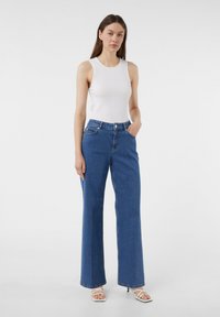 Witte geribde tanktop gecombineerd met hoog-waist, wijde blauwe denim jeans. De jeans zijn voorzien van zakken aan de voorkant en subtiele stiksels.