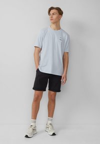 Lichtblauw shirt met korte mouwen en een logo op de borst, gecombineerd met zwarte shorts en witte sneakers. Eenvoudig ontwerp, ontspannen pasvorm.