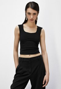 Top cropped nero con scollo quadrato in tessuto elasticizzato, abbinato a pantaloni neri a vita alta con pince e tasche laterali.