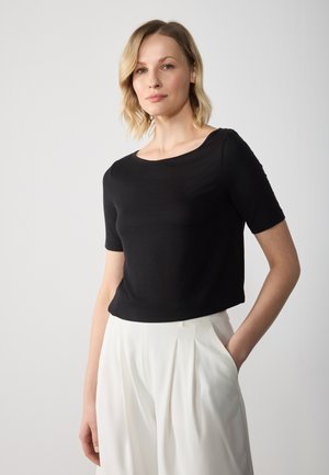 Černý krátký rukáv top z hladkého materiálu s kulatým výstřihem, v kombinaci s bílými skládacími kalhotami, které mají volný střih a minimalistický design.