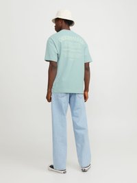 T-shirt bleu clair à manches courtes avec un design de texte au dos. Associé à un jean en denim clair et des baskets noires. Un chapeau seau blanc complète le look.