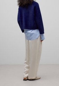 Marineblå fuzzy cropped sweater over en lyseblå skjorte, kombineret med cremegule vidde bukser og beige spidse flade sko.