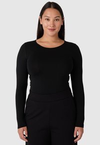 Musta pitkähihaiset paita, jossa on pyöreä pääntie, valmistettu sileästä kankaasta. Vartalonmyötäinen muotoilu, yhdistettynä korkeavyötäröisiin mustiin housuihin. Yksinkertainen ja tyylikäs.