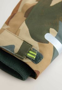Kamuflage-mønstret ærme med en grøn strikket manchet, der har en velcro-rem og en refleksdetalje. Fremstillet af et holdbart syntetisk materiale.