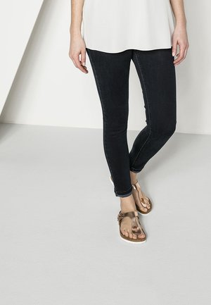 Jean skinny en denim foncé associés à des sandales à lanière en bronze métallique. Les sandales présentent un design à lanière et une semelle en liège avec des accents blancs.