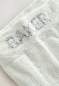 Primer plano de un puño de calcetín blanco con la palabra "BANNER" tejida en letras grises a lo largo del borde superior.