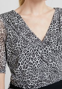 Leopardmönstrad topp med v-ringad halsringning, genomskinligt tyg och korta ärmar, med veckdetaljer vid bröstet och en solid svart midja.