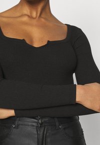 Czarny prążkowany top z długim rękawem i kwadratowym dekoltem, z lekkim wycięciem na środku. W zestawie z czarnymi spodniami z sztucznej skóry.