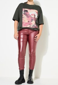 Olijfgroene oversized t-shirt met een kleurraf grafiek, gecombineerd met strakke bordeauxkleurige neplederen broek en zwarte chunky-zoled enkellaarsjes.