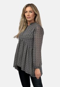 Czarna kwiatowa bluzka z przejrzystymi długimi rękawami, okrągłym dekoltem i marszczoną talią. Posiada subtelny wzór z małymi białymi kwiatami.