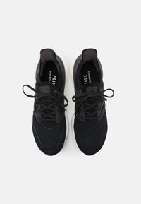 Zapatillas deportivas negras con una parte superior de malla transpirable, acentos texturizados, una suela blanca acolchada y cordones oscuros. Presenta la marca "PRIMEBLUE".