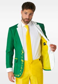 Giacca verde con colletto bianco e accenti gialli, caratterizzata da ricami decorativi. Pantaloni gialli e cravatta completano l'outfit. Interno foderato.