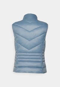 Jasnoniebieska kamizelka puchowa z wysokim kołnierzem, przeszyciami w kształcie zygzaka oraz poziomymi fałdami w talii, które nadają wyraźny kształt i teksturę.