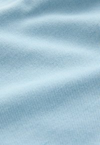 Gros plan sur un tissu en denim bleu clair montrant une fine texture de tissage diagonal et des plis subtils.