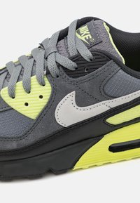Grey, black, and neon yellow Nike Air Max sneaker with textured laces, suede and mesh panels, and a white Nike swoosh logo.