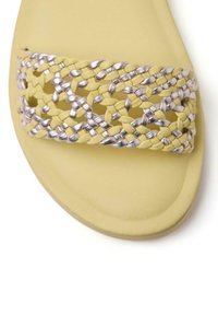 Sandale jaune avec une large bride tissée présentant des bandes entrelacées de cuir argenté et jaune sur le dessus.