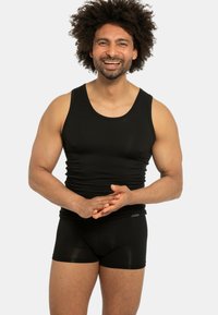 Canotta nera con scollatura a girocollo abbinata a boxer neri. Il tessuto appare liscio con un design aderente, che mette in risalto la fisicità.