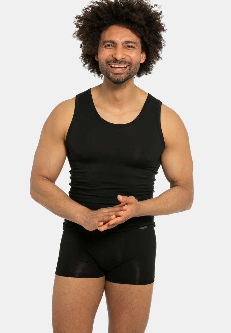 Canotta nera con scollatura a girocollo abbinata a boxer neri. Il tessuto appare liscio con un design aderente, che mette in risalto la fisicità.