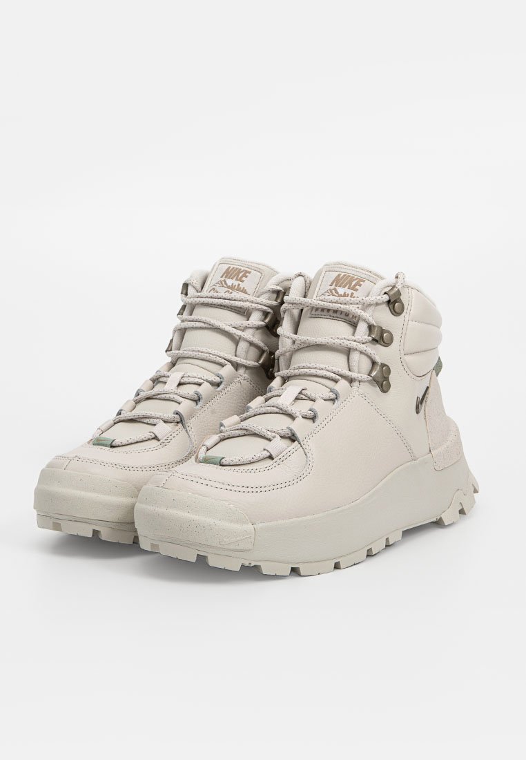 Zapatos altos de color beige claro con cuero texturizado, cuello acolchado y diseño de cordones. Cuentan con una suela de goma resistente con un diseño de relieve pronunciado para un mejor agarre.