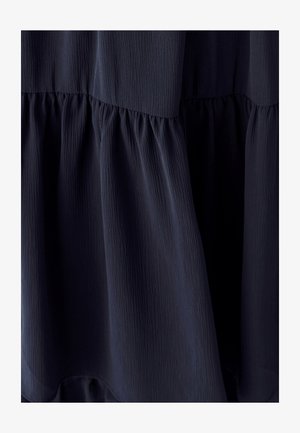 Námornícky modré tiered šaty s textúrovanou tkaninou. Obsahujú zberané detaily v páse a plynulý siluetu.