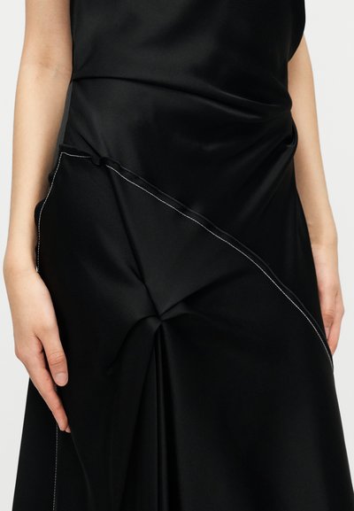 Abito in satin nero con dettaglio annodato, cucitura diagonale e impunture bianche a contrasto, che creano un aspetto elegante e strutturato.