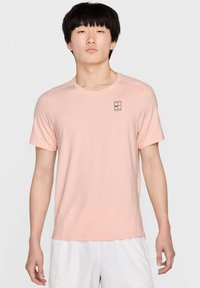 Camiseta atlética de color rosa claro, de manga corta, con escote redondo y un pequeño logo negro en el lado izquierdo del pecho. Tejido suave y transpirable.