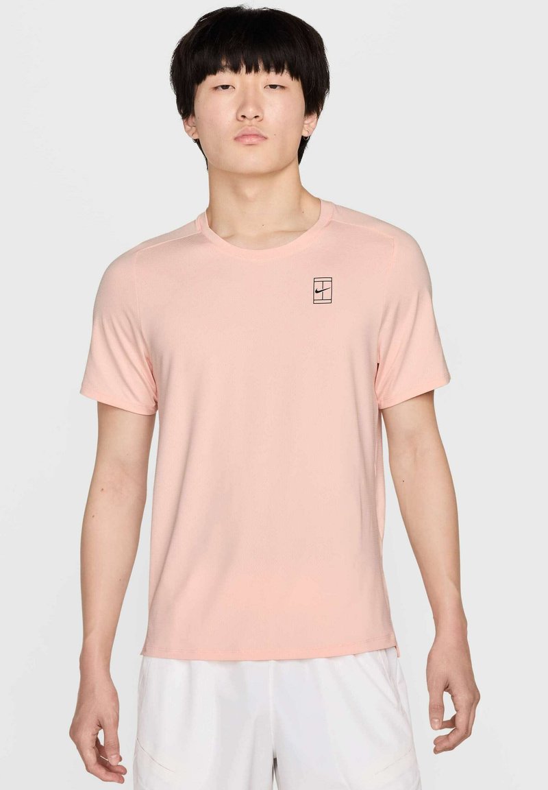Camiseta atlética de color rosa claro, de manga corta, con escote redondo y un pequeño logo negro en el lado izquierdo del pecho. Tejido suave y transpirable.